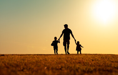silhouette of father and children holding hands walking outdoors in the park. Fatherhood, and childhood concept.  - Powered by Adobe