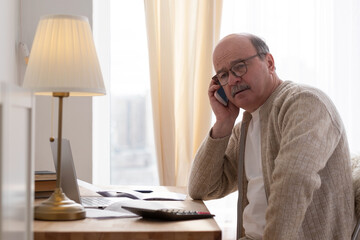 Senior man talking on phone sitting at table at home
