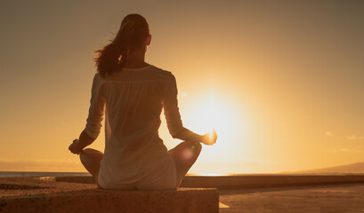 Female silhouette meditating at sunset in a calm relaxed state of mind.	