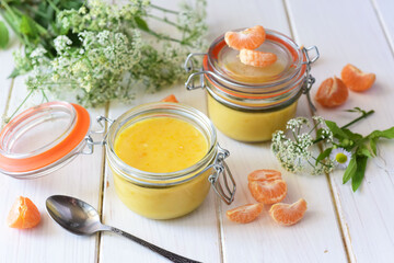 Delicate tangerine curd in a glass jar on a white table. Citrus cream.