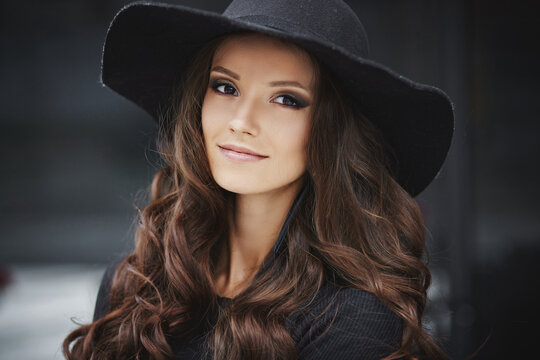 Closeup fashion portrait of a young model woman with trendy makeup wearing black fashionable hat posing outdoors
