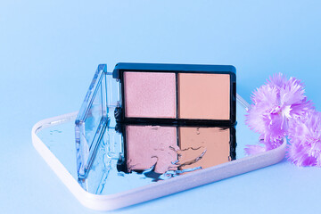 Artistic composition with make up blush on the mirror with waterdrops and flowers. Cosmetic branding background.