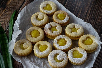 Linzer cookies with hearts, stars and moons with mango yellow curd (sauce) and powdered sugar on a old wooden background. Traditional dessert. Horizontal orientation.
