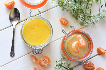 Sweet tangerine curd in a glass jar and tangerine slices on a white table.