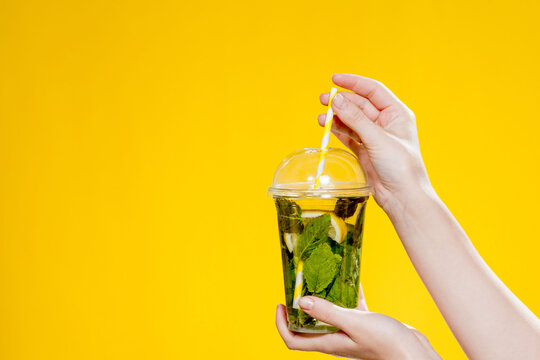 Mojito cocktail in a plastic glass with a tube on a yellow background. ool drink in the summer for takeaway. Place for text