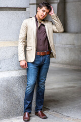 Fototapeta premium Dressing in a beige color blazer, a coffee color shirt, blue jeans, a scarf tied in the neck, and one hand touching his head, a handsome guy is charmingly looking at you