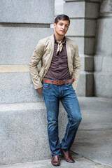 Dressing in a beige color blazer, a coffee color shirt, blue jeans, a scarf tied in the neck, and two hands putting on the back,  a handsome guy is standing outside and taking a break..