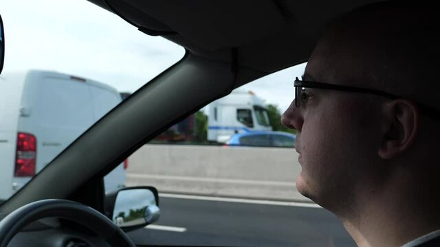 Side view of concentrated male driver face driving on a highway in the UK, man is wearing glasses.