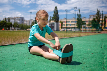 Cute preteen girl making exercises with fitness resistance band at public sportsground in the city, wellness and fitness, sport and recreations, healthy lifestyle - obrazy, fototapety, plakaty