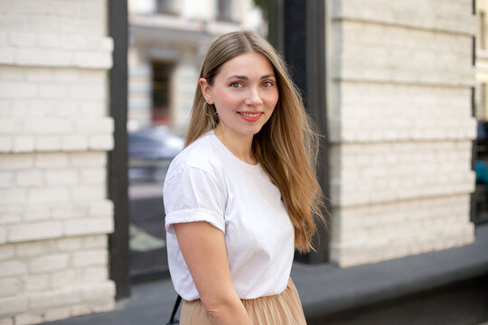 beautiful caucasian girl with blonde hair in a white t-shirt looks at the camera and smiles