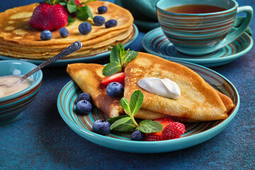 Pancakes with berries and sour cream on dark green background.  Maslenitsa. Shrovetide. Shrove Tuesday. Pancake Day.