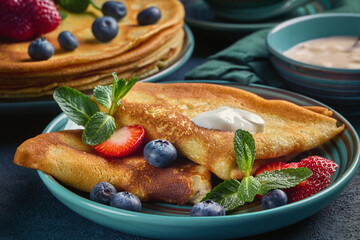 Pancakes with berries and sour cream on dark green background.  Maslenitsa. Shrovetide. Shrove Tuesday. Pancake Day.