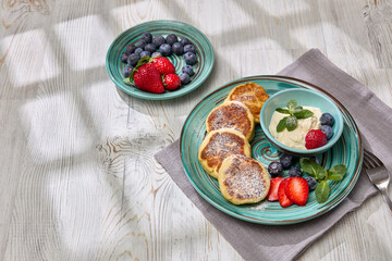 Russian cottage cheese pancakes (Syrniki) with berries and sour cream on light wooden background. Top view. Healthy breakfast