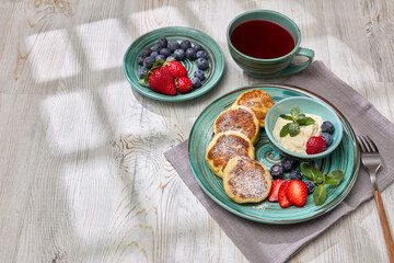 Russian cottage cheese pancakes (Syrniki) with berries and sour cream on light wooden background. Top view. Healthy breakfast