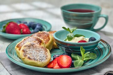 Russian cottage cheese pancakes (Syrniki) with berries and sour cream on light wooden background. Healthy breakfast