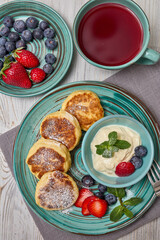 Russian cottage cheese pancakes (Syrniki) with berries and sour cream on light wooden background. Top view. Healthy breakfast
