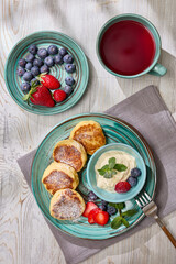 Russian cottage cheese pancakes (Syrniki) with berries and sour cream on light wooden background. Top view. Healthy breakfast