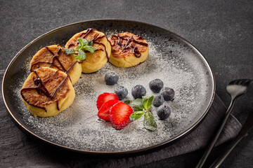 Russian cottage cheese pancakes (Syrniki) with berries and chocolate sauce on black background.