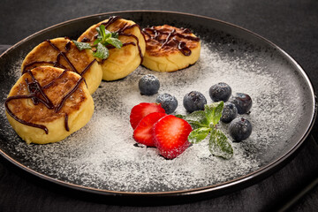 Russian cottage cheese pancakes (Syrniki) with berries and chocolate sauce on black ceramic  plate. Food background