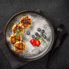 Russian cottage cheese pancakes (Syrniki) with berries and chocolate sauce on black background. Top view
