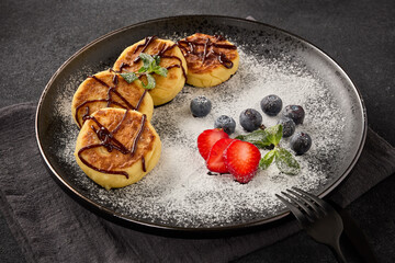 Russian cottage cheese pancakes (Syrniki) with berries and chocolate sauce on black background.