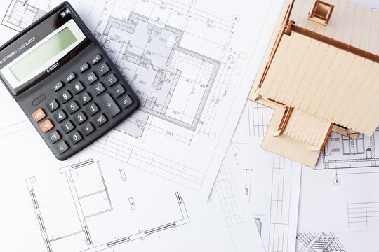 calculator and wooden house against the background of drawings