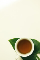 White mug of green tea on white background with leaf. Flat lay image with copy space.