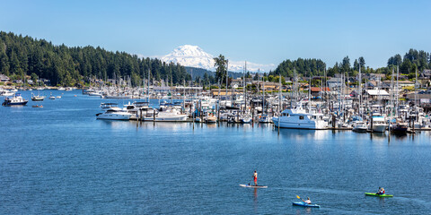 Fototapeta na wymiar Paddle boarders and kayaks in the Gig Harbor marina with mt rainier in the background