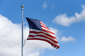 American flag flying in a breeze against a sunny blue sky with light white clouds
