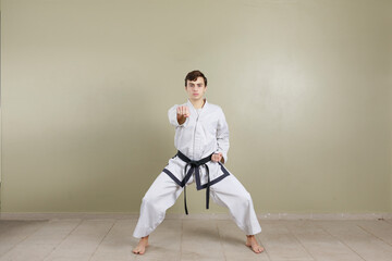 Young man from the front throwing a taekwondo fist punch. Dressed in dobok uniform with black belt. Isolated on light background and copy space for text.