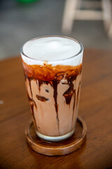 Close-up Iced cafe Mocha-Coffee with chocolate on top with milk creme serving in Ice in glass putting on the coaster and wooden table. Taken in selective spot focus to use as abstract Cafe background