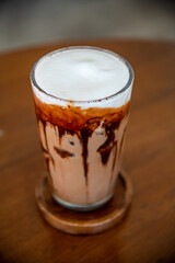 Close-up Iced cafe Mocha-Coffee with chocolate on top with milk creme in Ice in glass putting on the coaster and wooden table. Take in top view, selective spot focus to use as abstract Cafe background