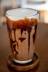 Close-up Iced cafe Mocha-Coffee with chocolate on top with milk creme serving in Ice in glass putting on the coaster and wooden table. Taken in selective spot focus to use as abstract Cafe background