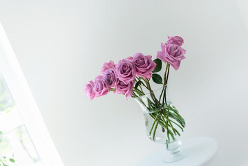 a bouquet of pink roses in a transparent vase against a white wall with a littered horizon