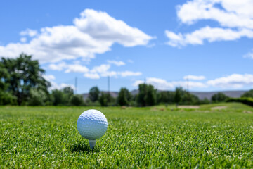 White golf ball sitting on a white tee in the tee box, hole long way in the distance
