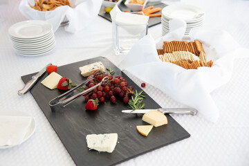 Cheese board with different kinds of cheese, grapes, strawberry on a table. Wedding or party catering. Copy space for your text