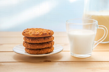 A glass of milk with cookies on a wooden table.