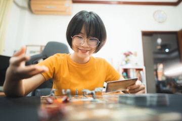 Happy young adult asian woman playing board game on top table at home eye looking camera.