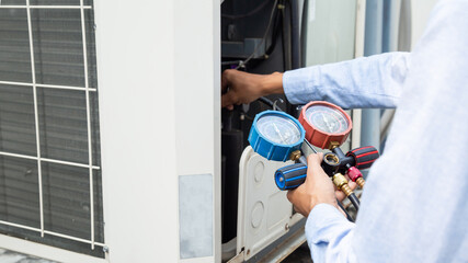 Air repair mechanic using measuring equipment for filling industrial factory air conditioners and...