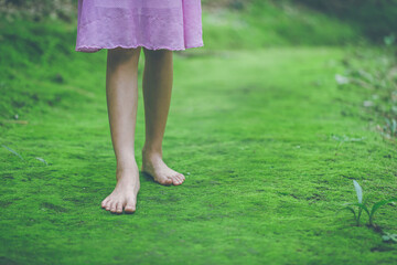 little girl bare feet walking on green moss in forest trail
