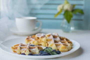 Waffles for breakfast. Belgian or Viennese waffles with berries on a white ceramic plate with a cup of aromatic coffee. 