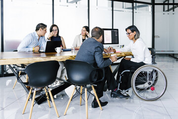Latin handicapped transgender woman with business people working on computer and documents at office desk, in disability concept and disabled people