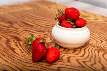 ripe juicy red strawberries in a cup and on a wooden table