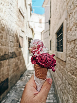 Personal Perspective Of Male Hand Holding Ice Cream Cone With Two Scoops Of Ice Cream In Street.