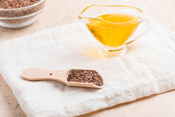 Flax seed oil and flax seed in spoon and napkin are on beige stone background