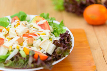 Mixed fresh vegetables salad in white dish on wood plate