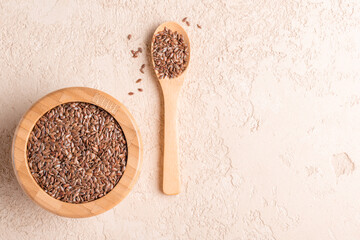 Flax seed is in a wooden bowl and spoon on beige stone background. Flat lay. Copy space.