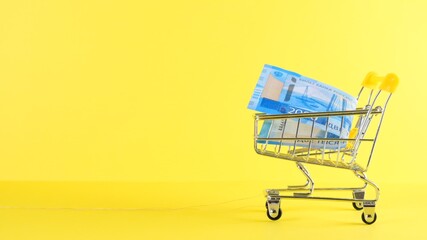 Shopping cart with 2000 rubles banknote on a yellow background, closeup. Black Friday Shopping and Discount Concept