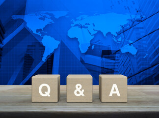 Q and A letter on block cubes on wooden table over world map, modern office city tower and...