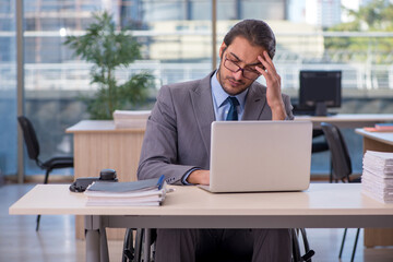 Obraz premium Young male employee in wheel-chair working in the office